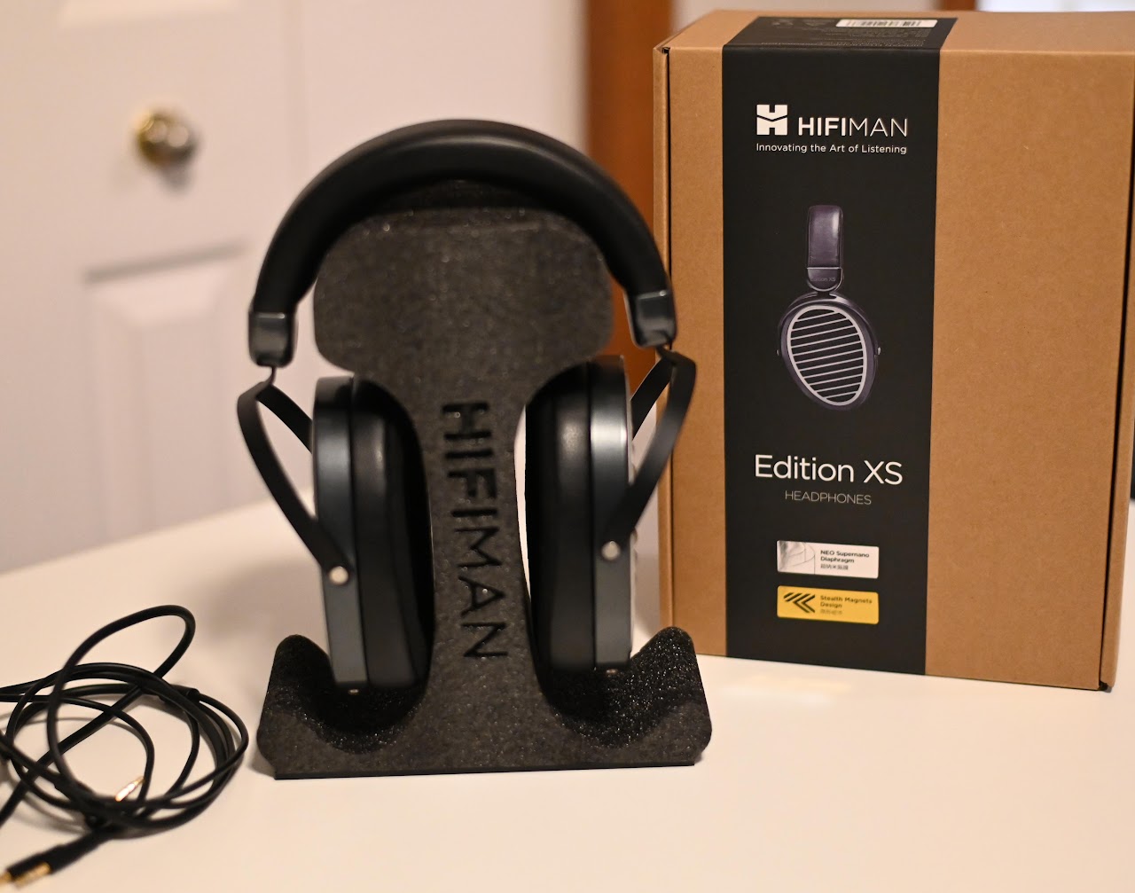 Rear view of Hifiman Edition XS headphones on a foam stand beside their box